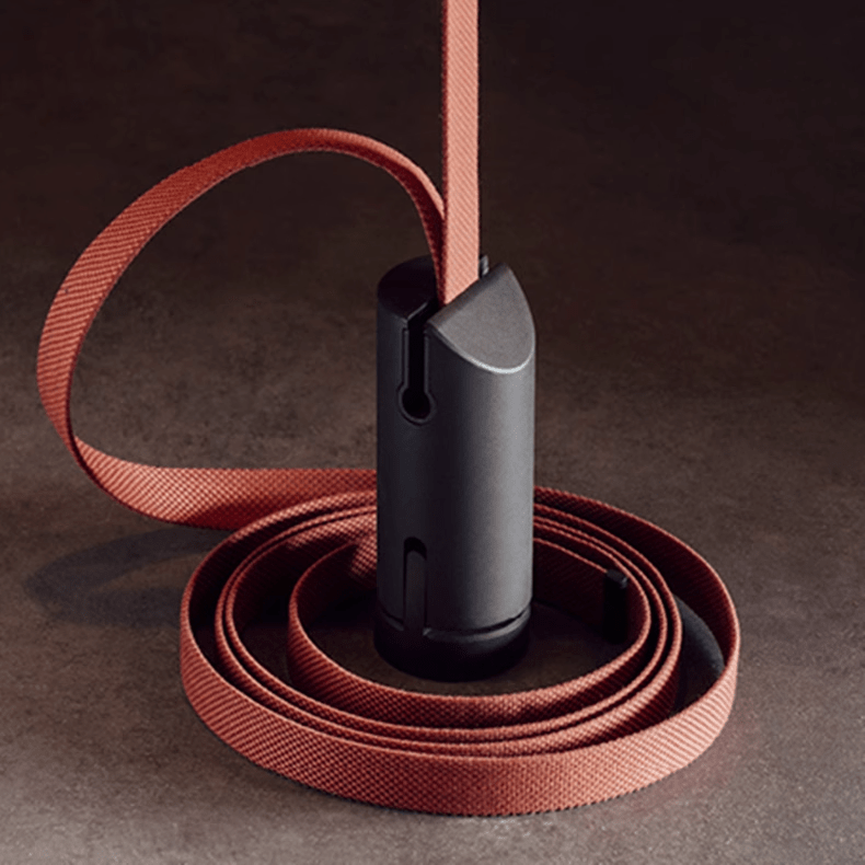 Close view of the red woven strap coiled around a dark metal cylinder, the cable housing of this Clérachic linear pendant light.