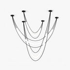 Black Clérachic linear pendant of several draped cords from ceiling canopies, with curved white LED tubes hanging between them, on white.