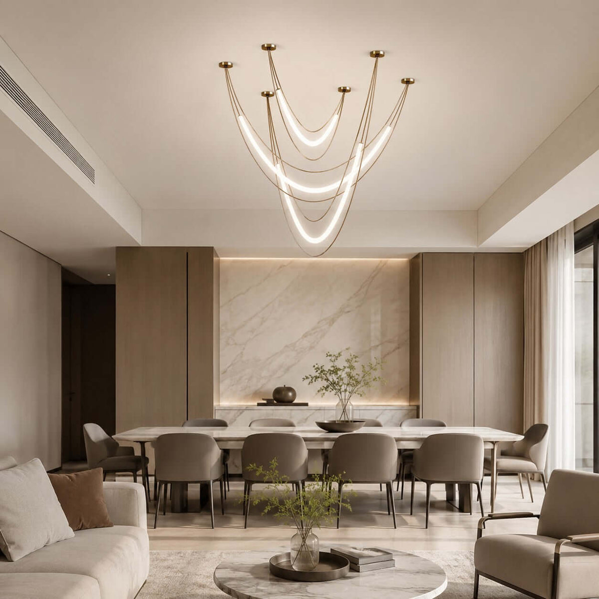 Gold and white Clérachic pendant cluster of lit curved tubes above a long dining table in a marble-panelled room with taupe chairs.