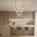 Gold Clérachic pendant with layered glowing curves hung over a marble kitchen island with gold-legged bar stools.