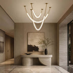Clérachic gold pendant with three lit hammock-shaped tubes in an entry hall, a curved stone console and a large abstract canvas below.
