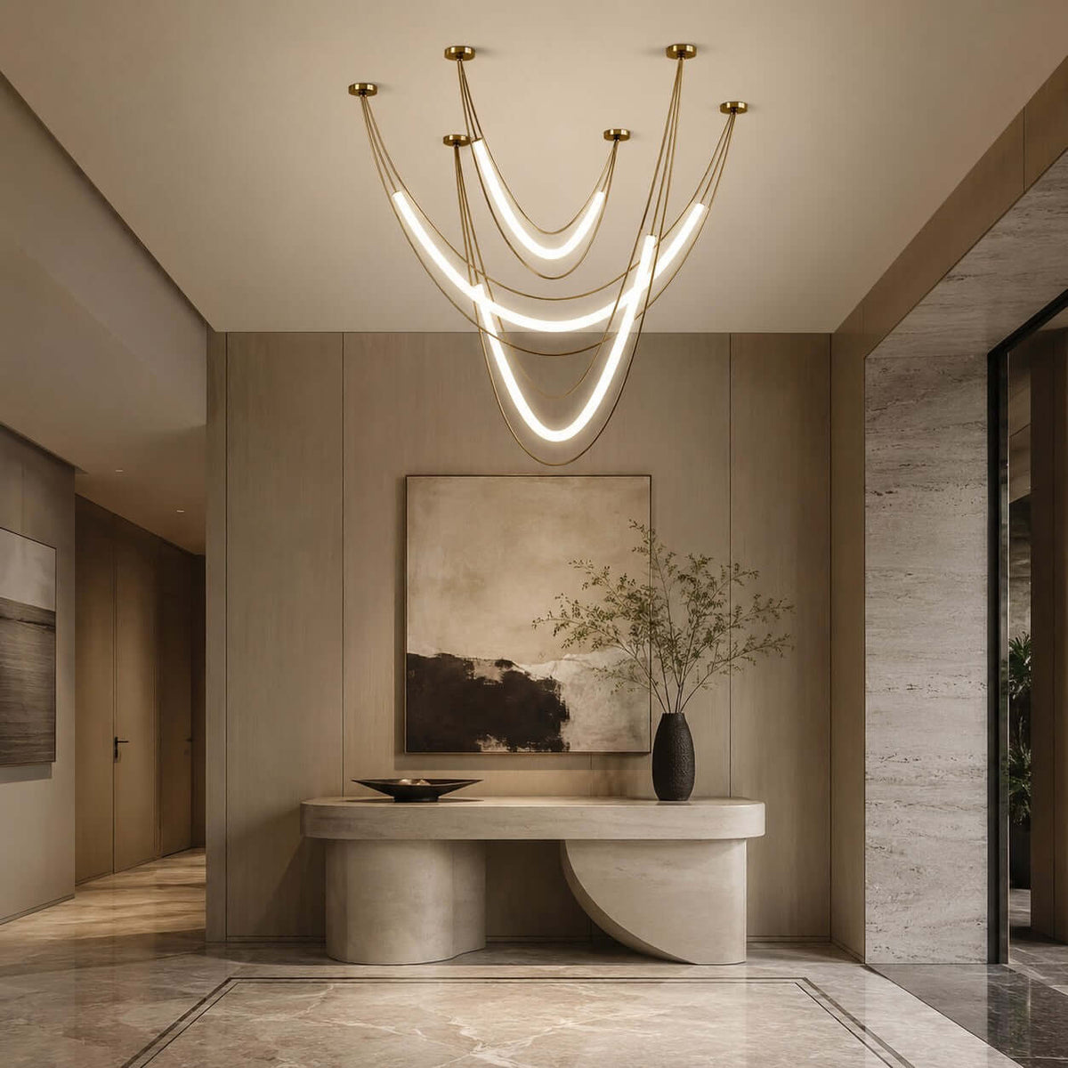 Clérachic gold pendant with three lit hammock-shaped tubes in an entry hall, a curved stone console and a large abstract canvas below.