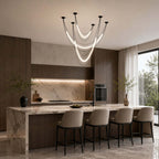 Lit black Clérachic pendant cluster above a stone kitchen island with four black-legged stools, tall windows to one side.