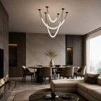 Black Clérachic cluster of glowing curved tubes in a double-height room, a round dining table beyond a low sofa.