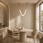 Lit gold Clérachic curved pendant over a round fluted-base table with two cream chairs, in a room with an arched alcove.