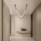 Black Clérachic pendant with a softly glowing tube, hung at a hallway junction before a floating stone shelf and a stone bowl.