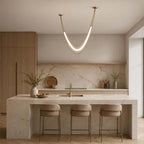 Gold Clérachic curved pendant above a stone-fronted kitchen island with three cushioned stools, oak cabinets behind.