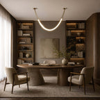 Gold and white Clérachic pendant glowing above a round wooden table in a study with lit bookshelves either side.