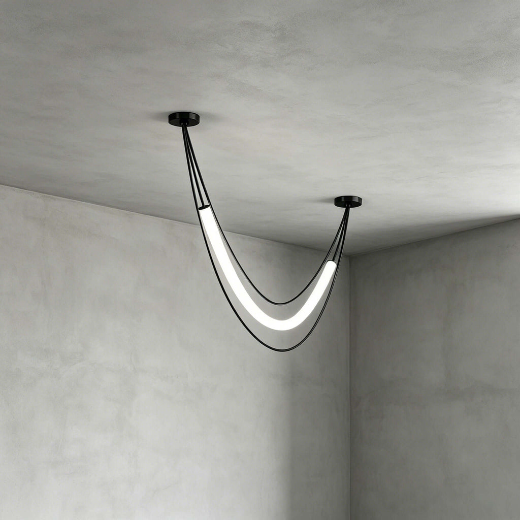 Black Clérachic pendant with one lit white curved tube and two cords, seen close in the corner of a concrete-look room.