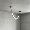 Black Clérachic pendant with one lit white curved tube and two cords, seen close in the corner of a concrete-look room.