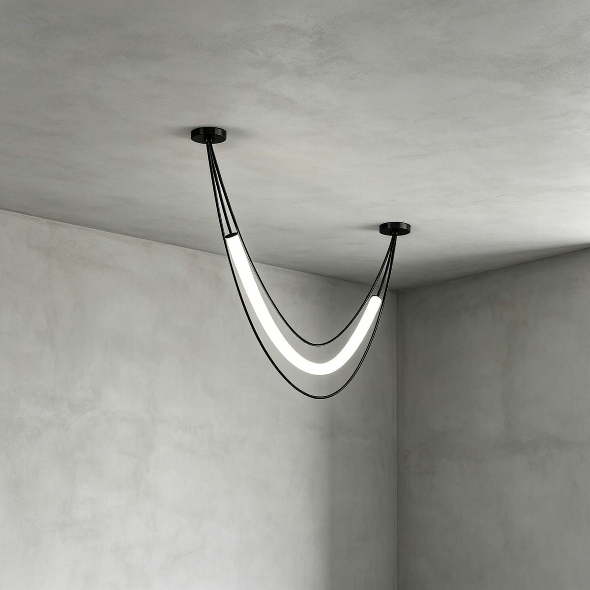 Black Clérachic pendant with one lit white curved tube and two cords, seen close in the corner of a concrete-look room.