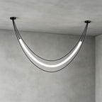 Black Clérachic pendant in its widest curve, a glowing tube between two ceiling canopies, against grey plaster walls.
