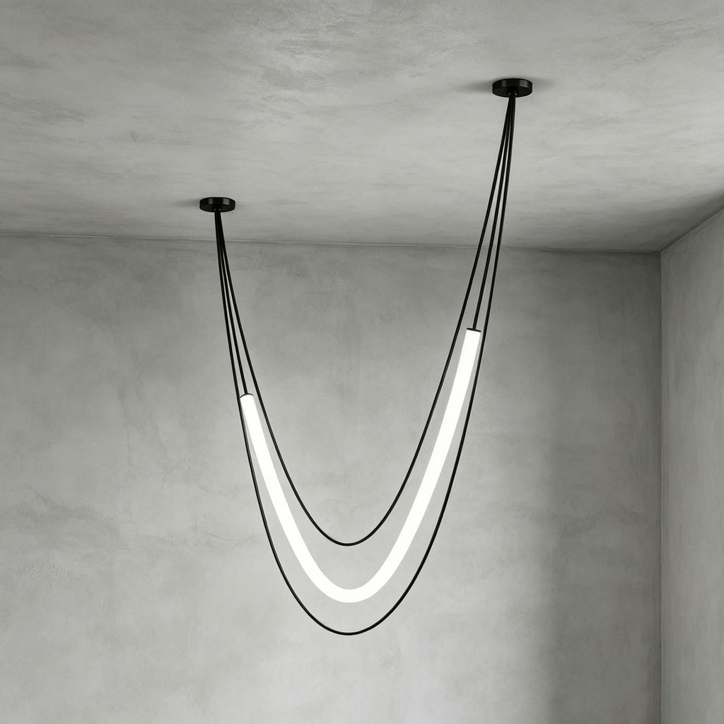 Deep, narrow black Clérachic pendant with its lit tube hanging low from uneven ceiling points, against grey plaster walls.