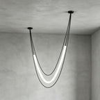 Deep, narrow black Clérachic pendant with its lit tube hanging low from uneven ceiling points, against grey plaster walls.