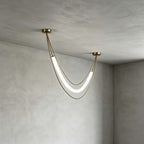 Compact gold Clérachic pendant with a lit white tube and fine gold cords, hung in a plaster-walled corner.