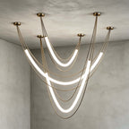 Gold Clérachic arrangement of three lit tubes on gold cords from five canopies, against a grey plaster corner.