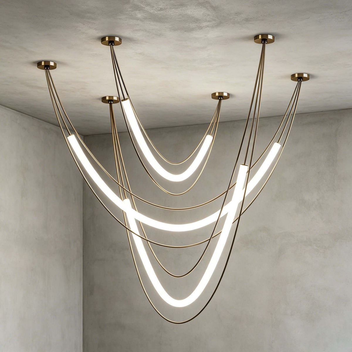 Gold Clérachic arrangement of three lit tubes on gold cords from five canopies, against a grey plaster corner.