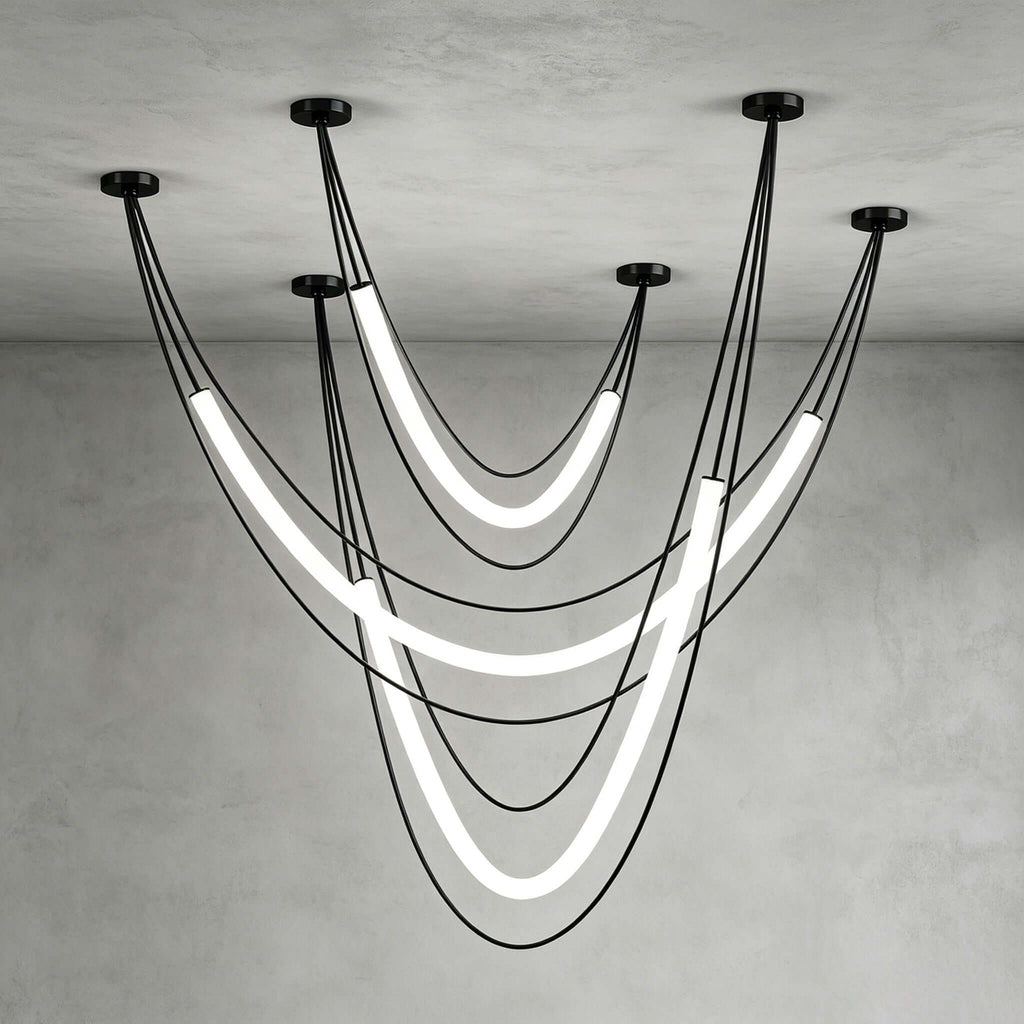 Black Clérachic arrangement of three glowing tubes on black cords from five ceiling canopies, against a grey plaster corner.
