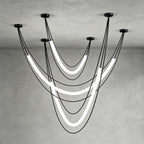 Black Clérachic arrangement of three glowing tubes on black cords from five ceiling canopies, against a grey plaster corner.