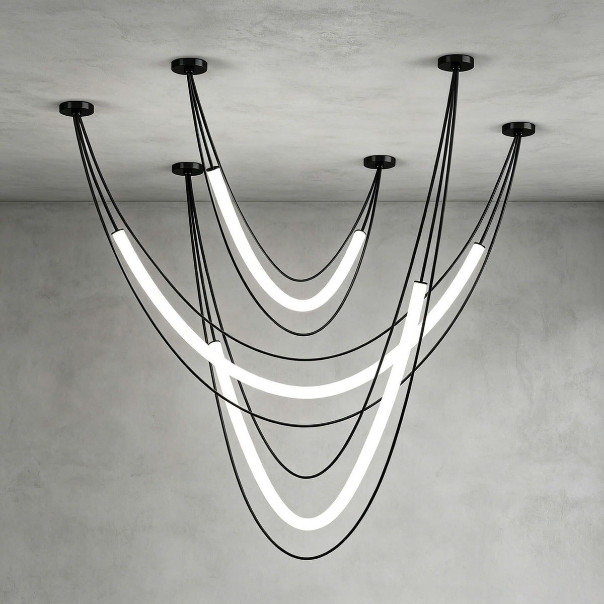 Black Clérachic arrangement of three glowing tubes on black cords from five ceiling canopies, against a grey plaster corner.