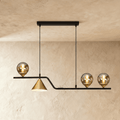 Clérachic linear pendant, a black bar with three glass globes and a gold cone shade, hung on two cords in a studio.