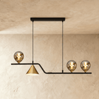 Clérachic linear pendant, a black bar with three glass globes and a gold cone shade, hung on two cords in a studio.