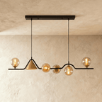 Clérachic wavy linear pendant on a black bar, with amber glass globes and a gold cone shade, in a studio on a limewash wall.