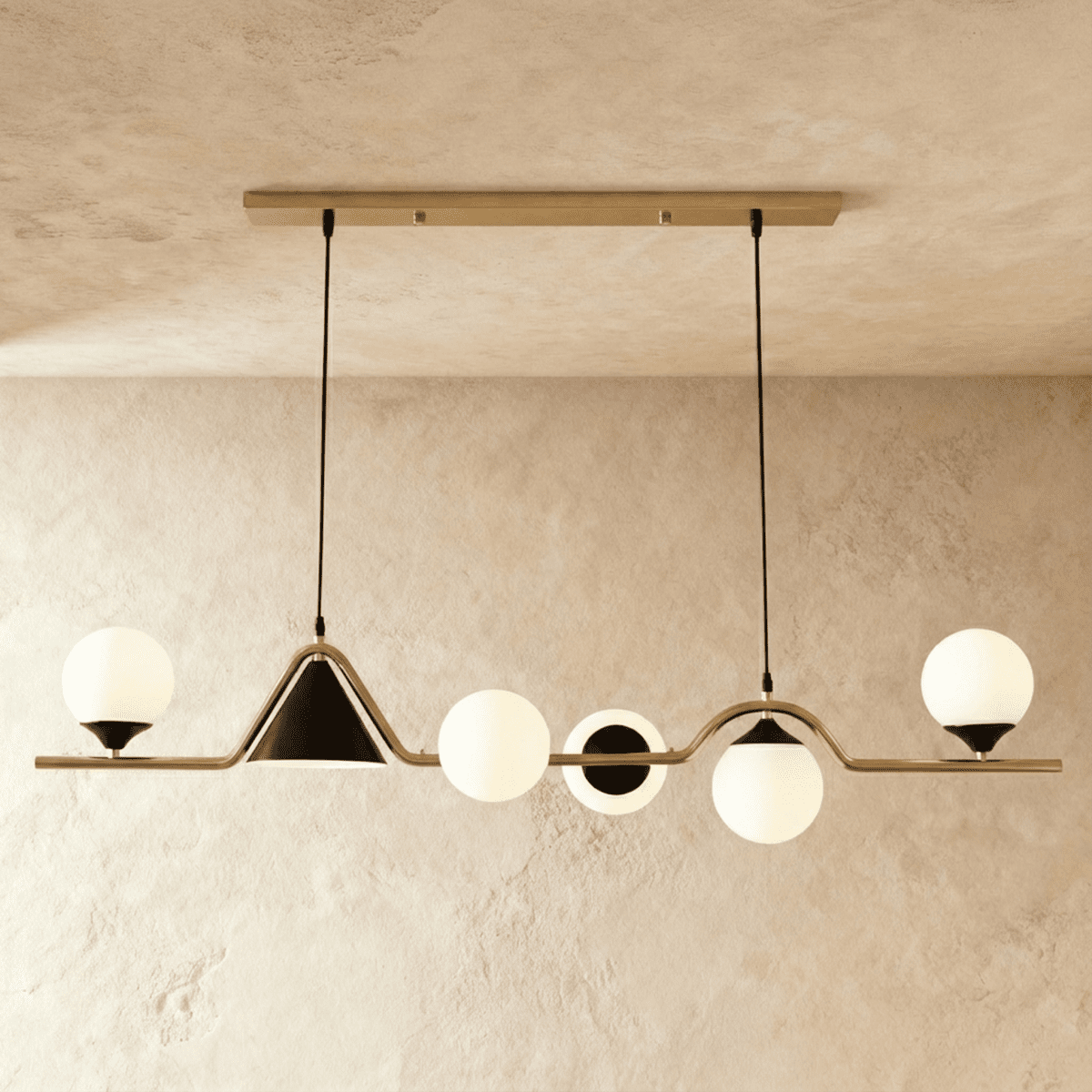 Clérachic wavy linear pendant with a gold bar, milk white glass globes and a black cone shade, studio shot on a limewash wall.