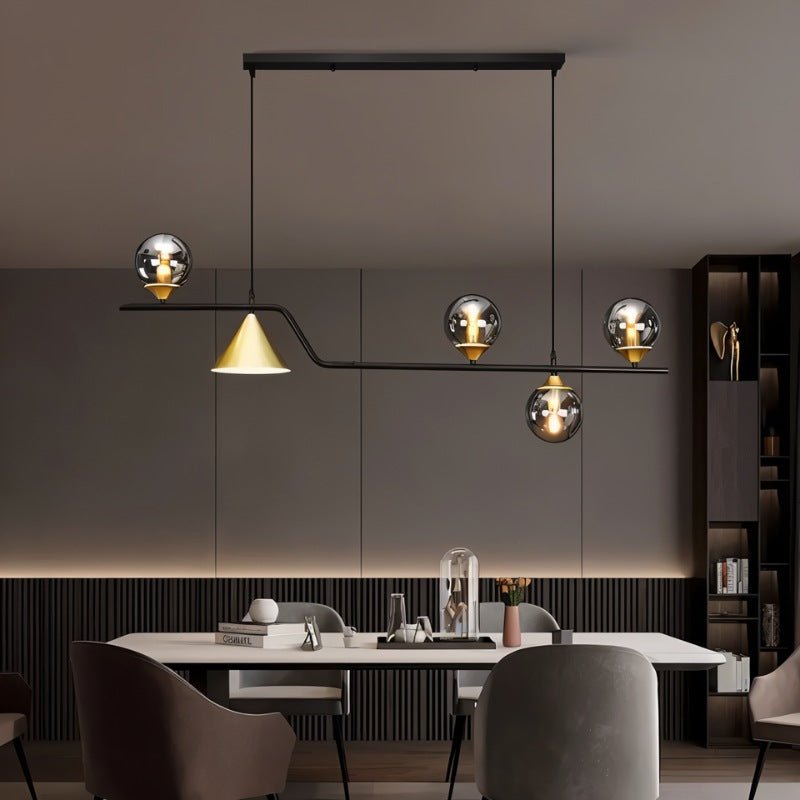 Clérachic black linear pendant with smoky glass globes and a gold cone shade, hung over a dining table in a room.