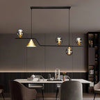 Clérachic black linear pendant with smoky glass globes and a gold cone shade, hung over a dining table in a room.