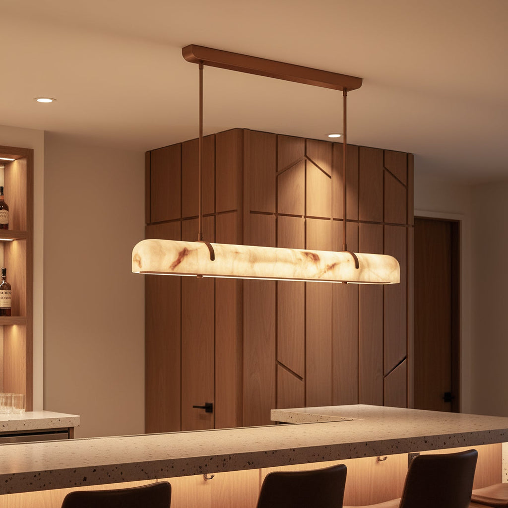 A glowing Clérachic linear pendant hangs in a kitchen bar area, with a speckled counter and a timber-panelled wall behind.