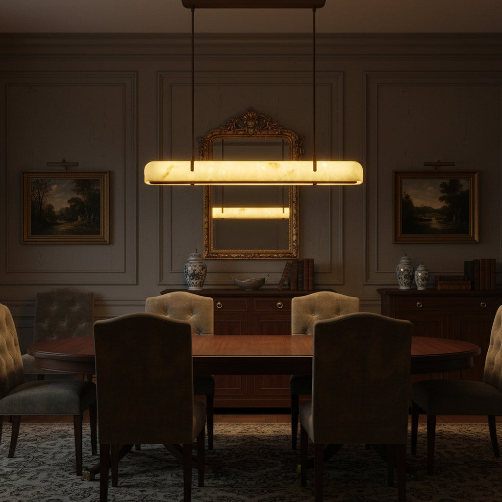 A lit Clérachic linear pendant hangs over a dark dining table, below a gilt mirror and landscape paintings.
