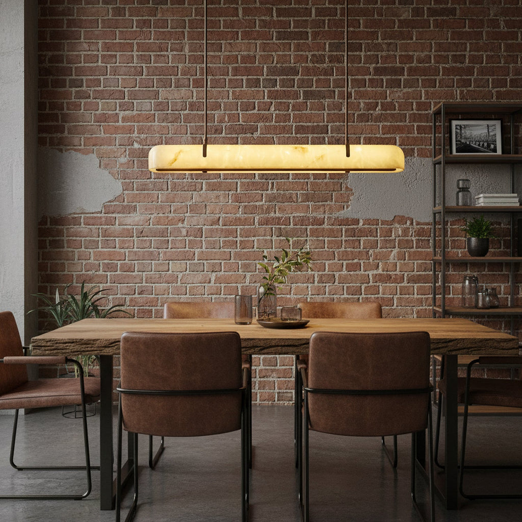 A lit Clérachic linear pendant hangs against a brick wall, above a rustic wooden table with leather chairs.