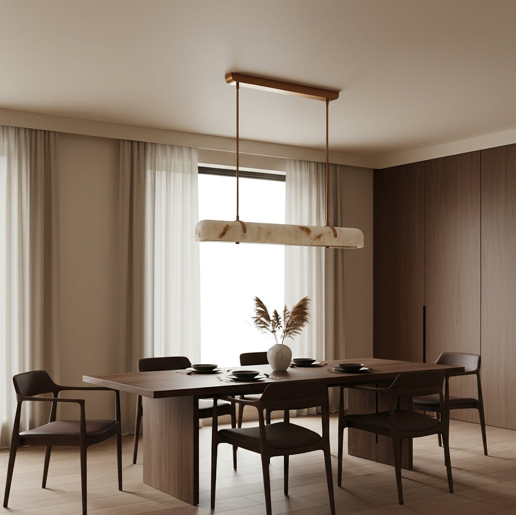 An unlit Clérachic linear pendant hangs in front of a window with sheer curtains, over a long table with dark chairs.