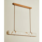 An unlit Clérachic linear pendant with copper-toned rods and a marbled white shade, against a warm cream wall.