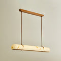 A Clérachic linear pendant glows on a warm beige backdrop, with the light showing through the shade.