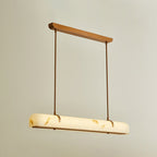 A Clérachic linear pendant glows on a warm beige backdrop, with the light showing through the shade.