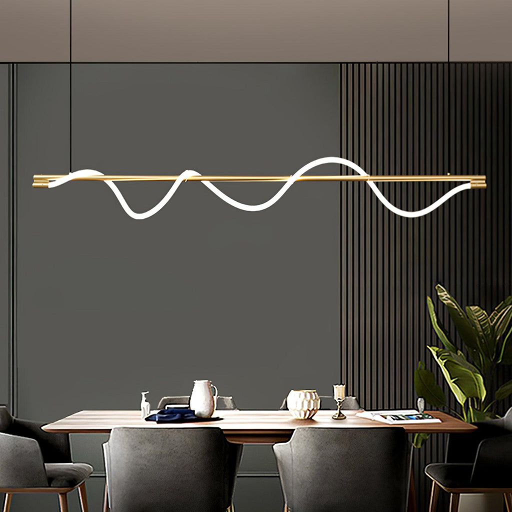 Brass Clérachic linear pendant with a glowing wave, above a wood dining table in front of a grey slatted wall.