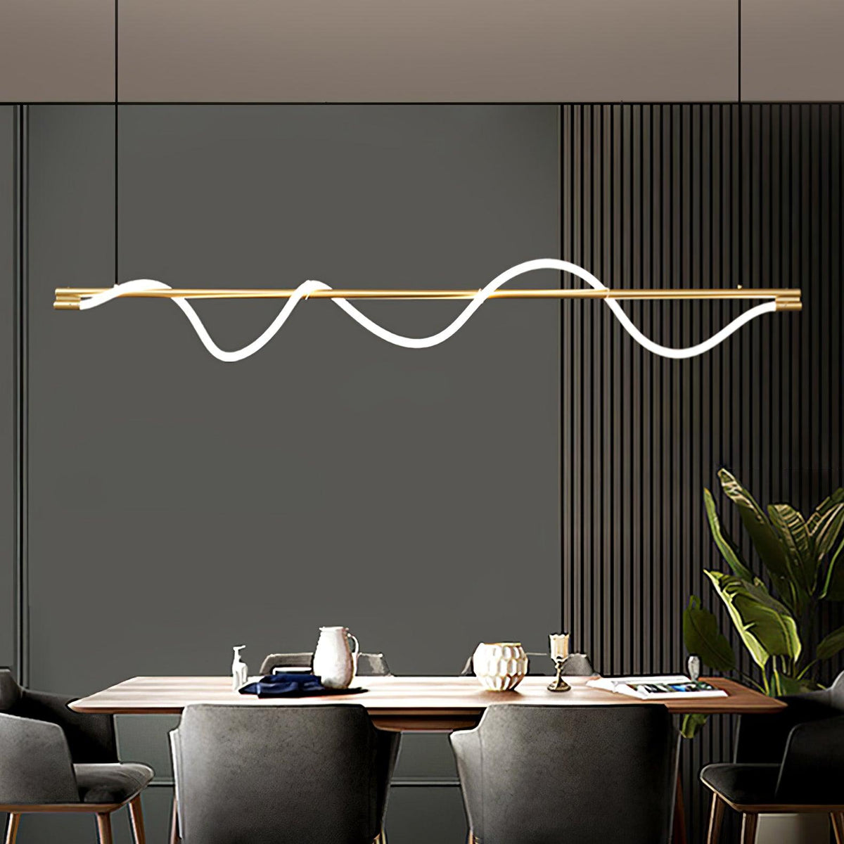 Brass Clérachic linear pendant with a glowing wave, above a wood dining table in front of a grey slatted wall.