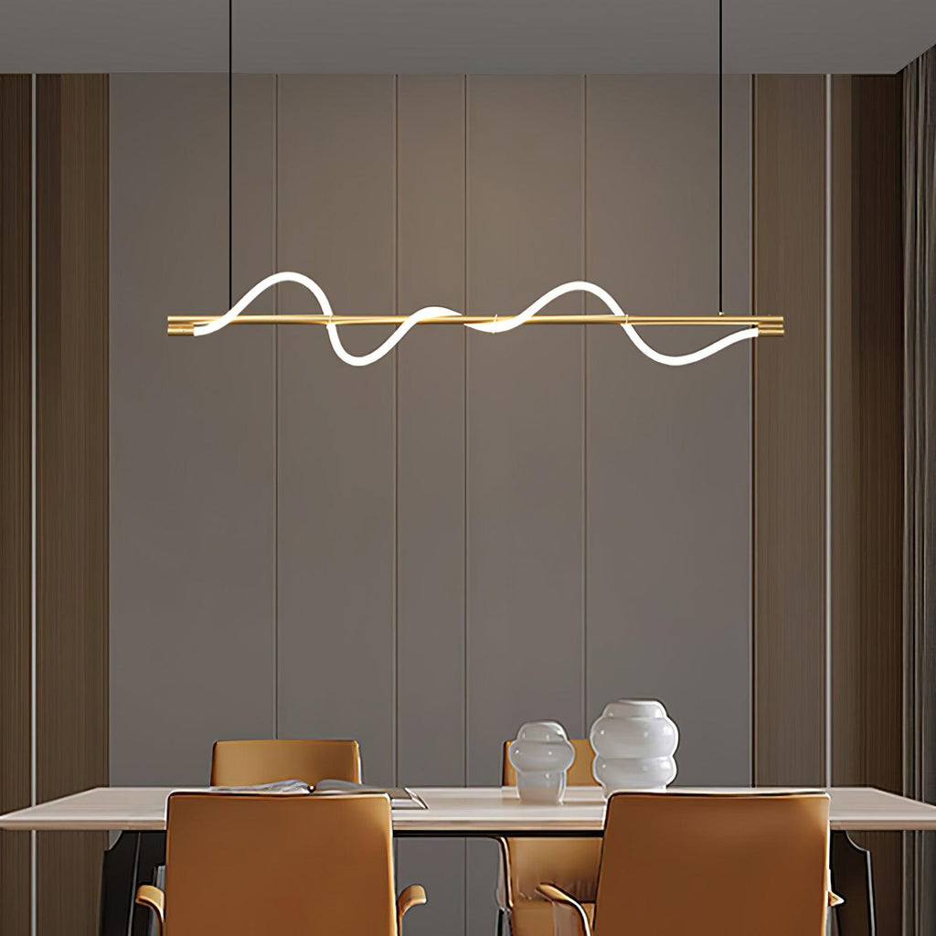 Lit brass Clérachic linear pendant above a pale table with tan chairs, against a warm taupe panelled wall.