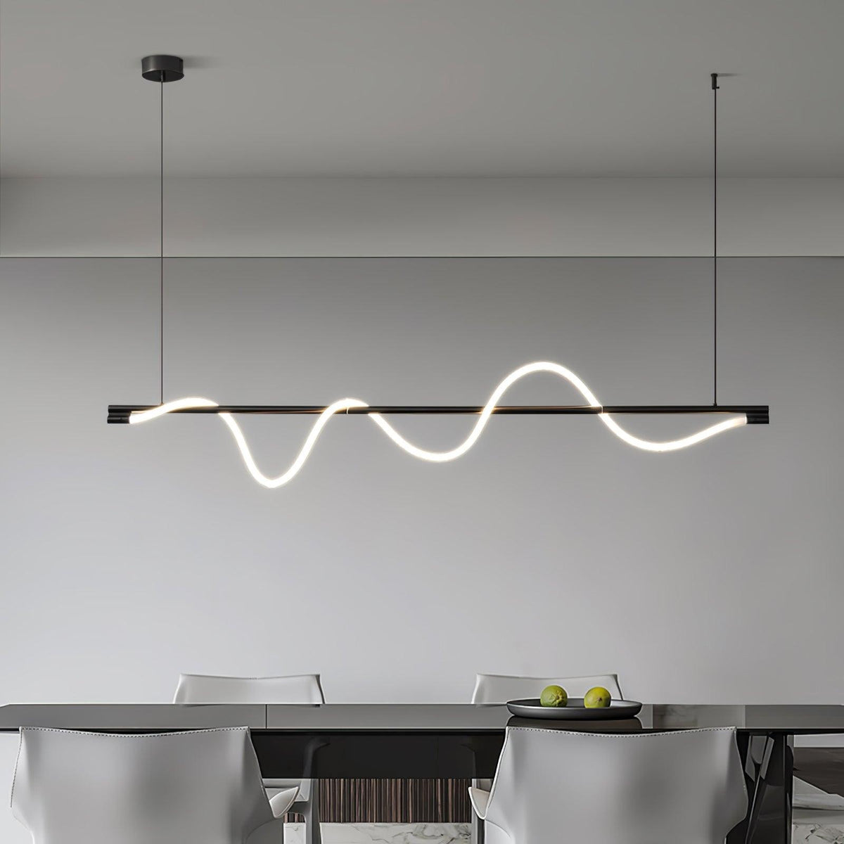 Wide black Clérachic linear pendant with a deep, glowing wave, hanging over a dark table with a bowl of limes.