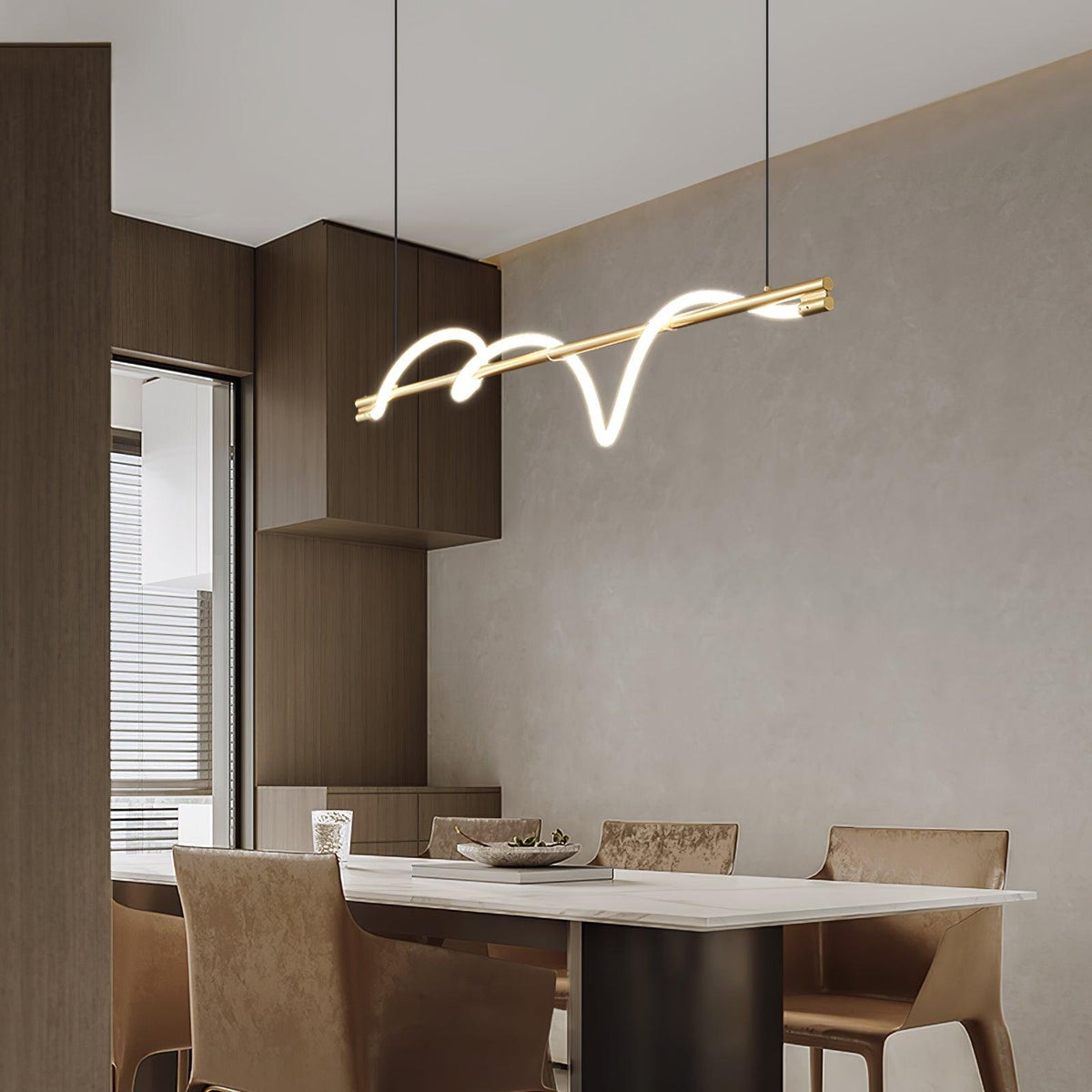 Slanted brass Clérachic linear pendant above a pale stone table and tan chairs, with wooden cabinets beside it.