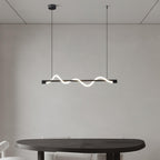 Clérachic black linear pendant with a low glowing wave over a rounded dark table, on a plain grey wall.