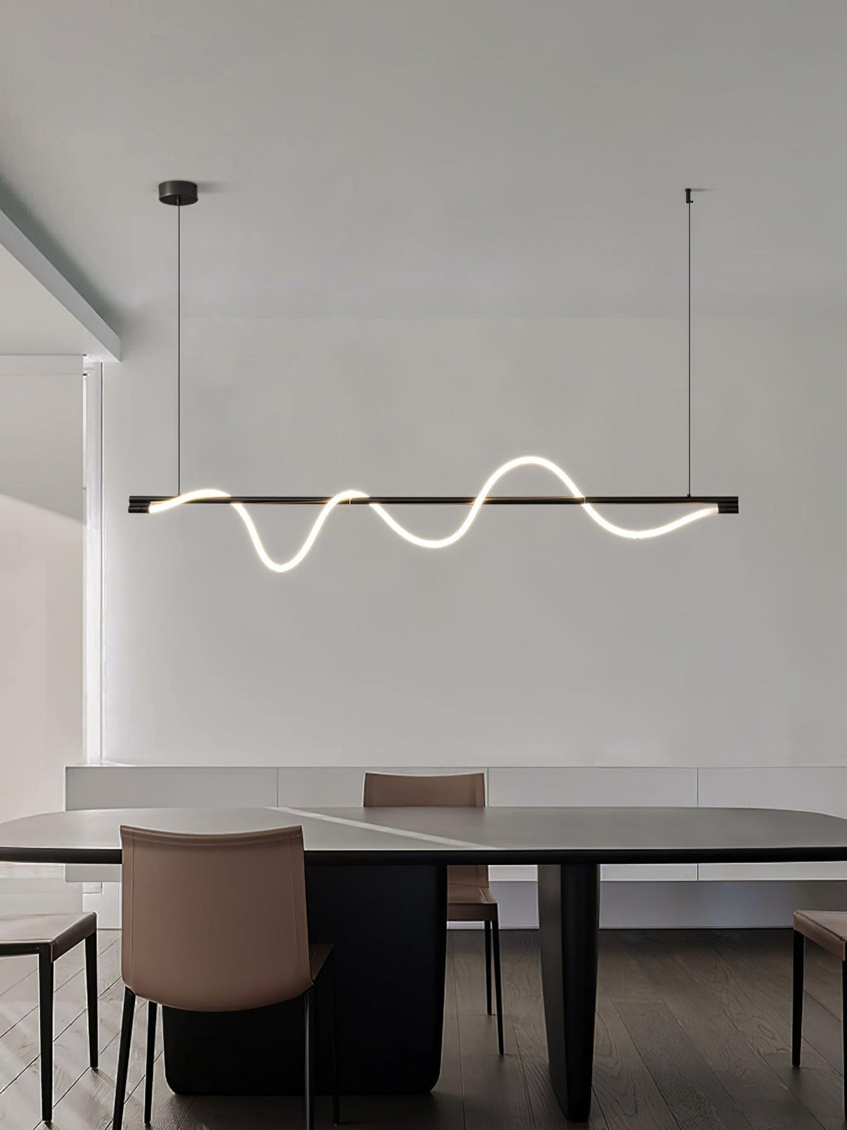 Side-angled view of a black Clérachic linear pendant lit above a dark table with a tan leather chair.