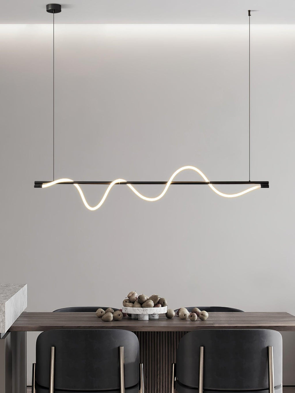 Black Clérachic linear pendant with a glowing wave, hanging above a walnut table set with a bowl of nuts and dark chairs.