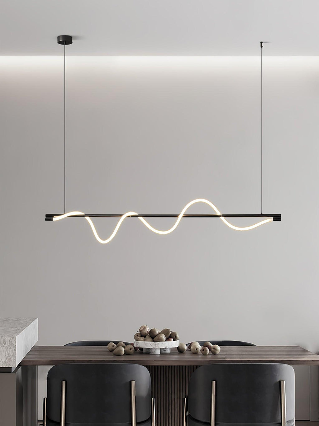 Clérachic black linear pendant seen against a cove-lit wall, over a table with a bowl of nuts and dark chairs.