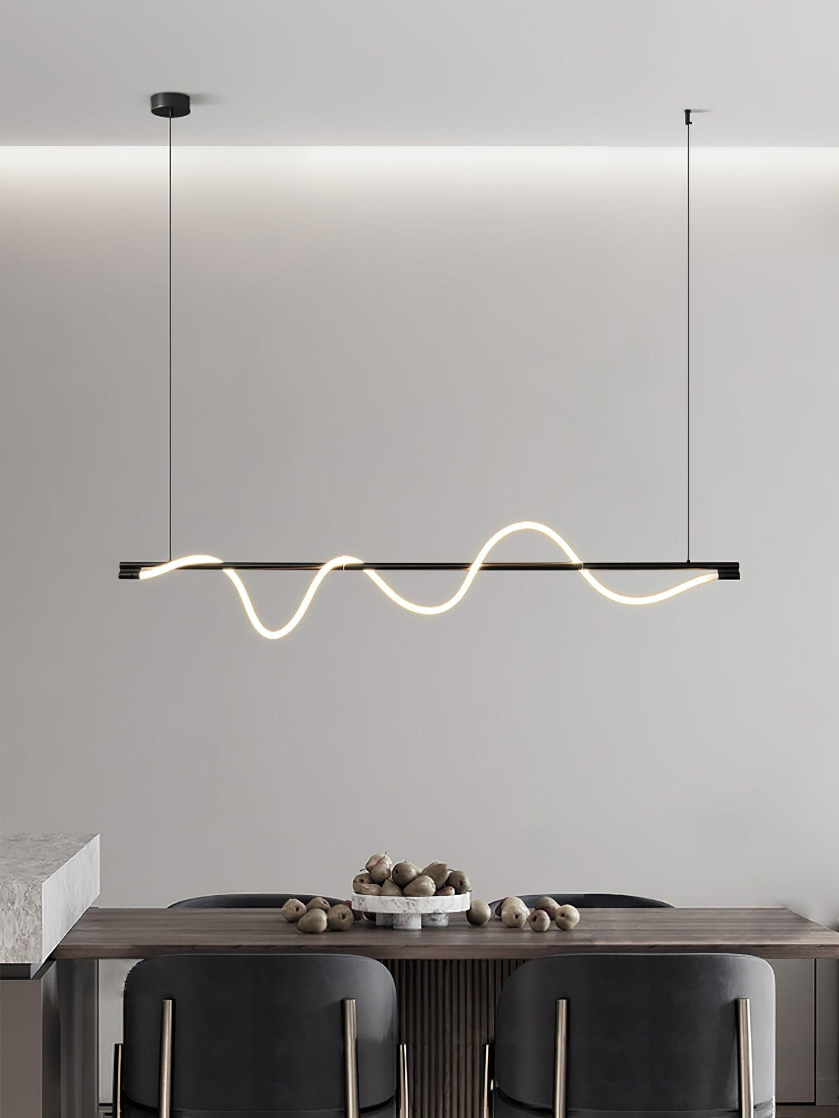 Clérachic black linear pendant seen against a cove-lit wall, over a table with a bowl of nuts and dark chairs.