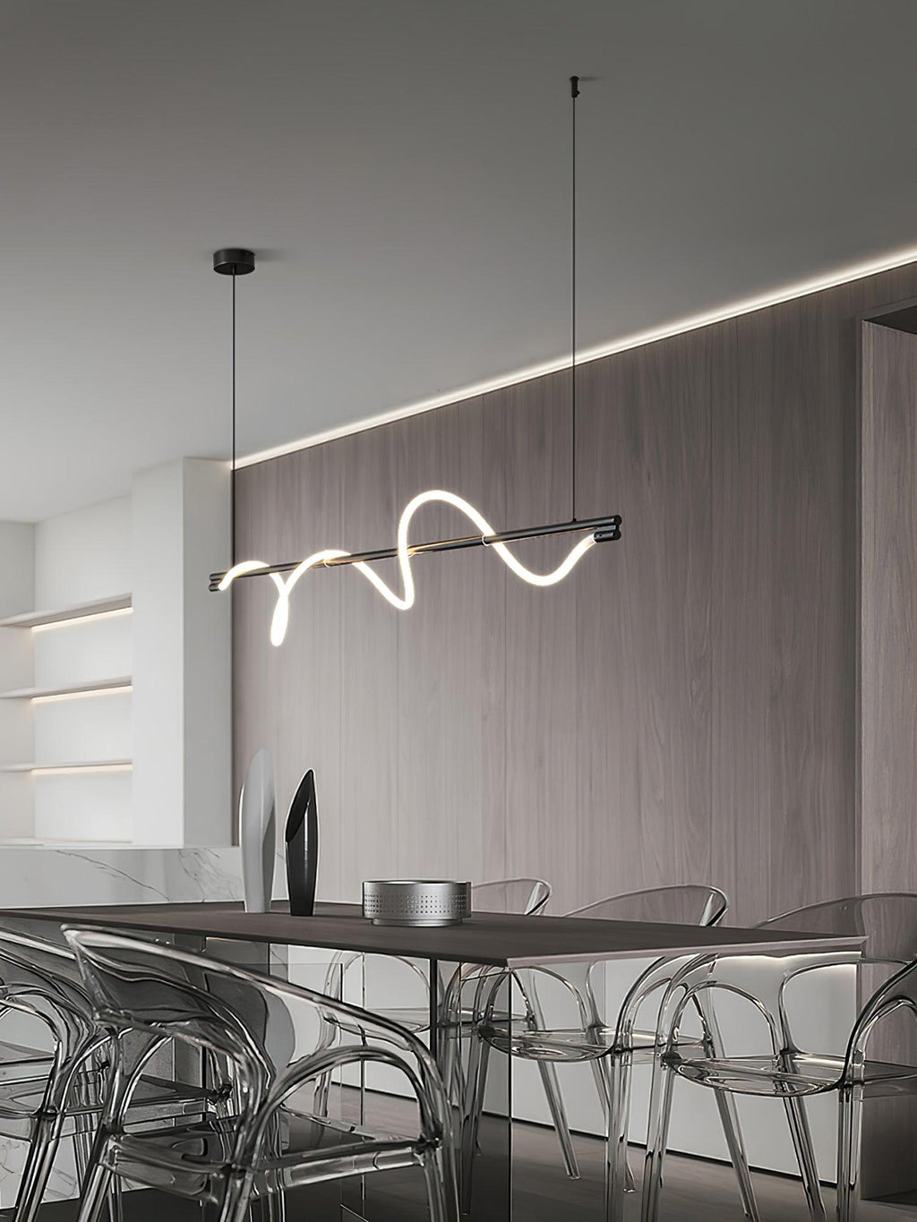 Black Clérachic linear pendant hung low in a dining room with a wood wall, a cove light and clear acrylic chairs.