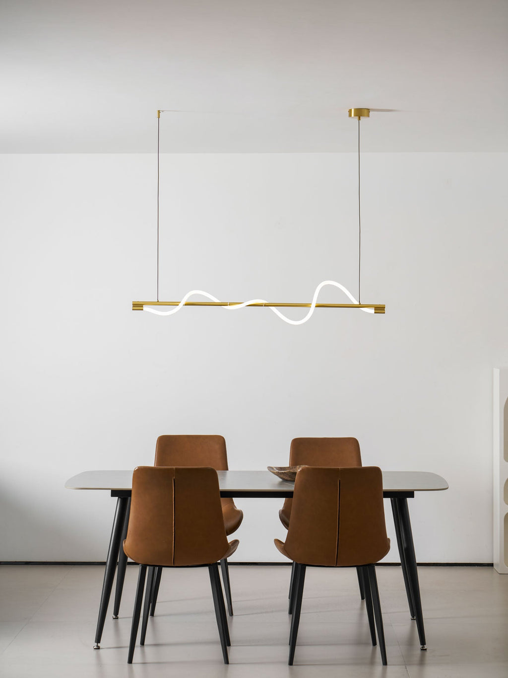 Clérachic brass linear pendant with a thin white line, hung high over a table with four rust-coloured chairs.