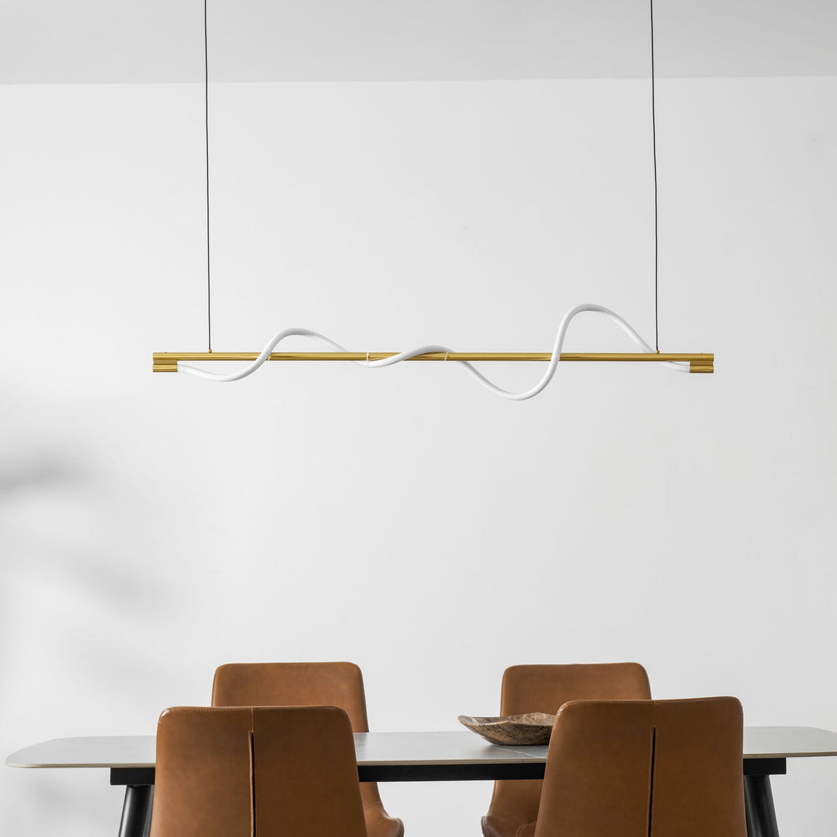Clérachic brass linear pendant with a white line, seen close above leather chairs and a wooden bowl on a table.
